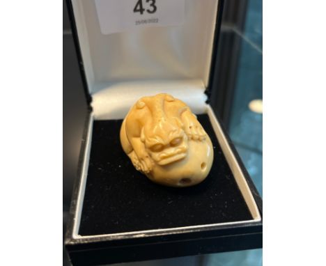 A Japanese hand carved tagua nut netsuke in the form of a foo dog gripping onto a rock. [4cm in length] 