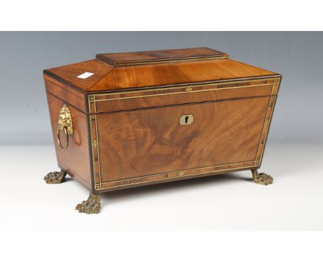 A Regency mahogany and brass inlaid tea caddy of sarcophagus form, raised on cast brass claw feet, width 30.5cm.Buyer’s Premi