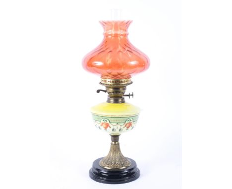 A late 19th century oil lamp with enamelled yellow glass body and cranberry shade, with Duplex burner, on gilt metal reeded s