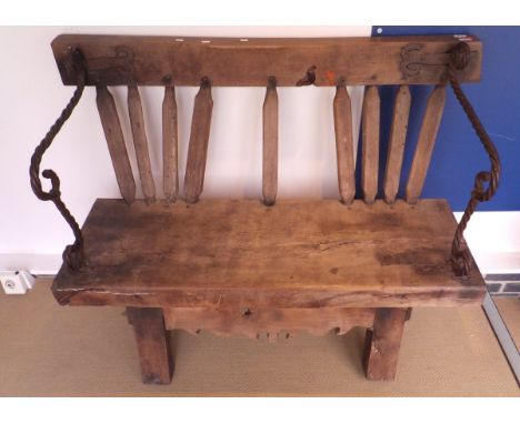 A rustic oak bench made from various parts with iron hand and arm rests