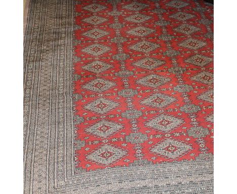 A Bokhara carpet , the central pattern set with repeating diamond shaped medallions on a red ground, within a stepped grey, b