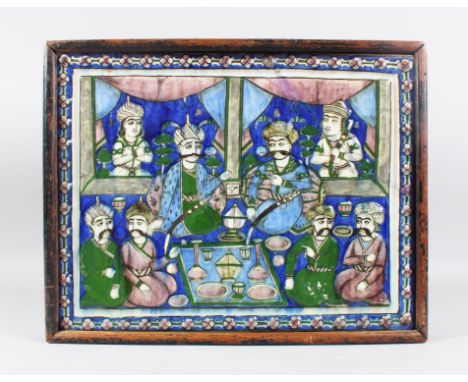 A 19TH CENTURY PERSIAN QAJAR GLAZED POTTERY TILE, painted with figures gathered in a palace, 36cm x 46cm in a wooden frame.