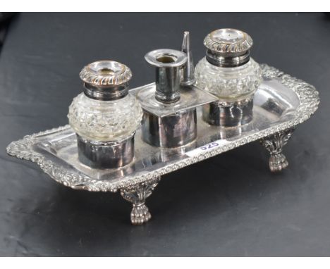 A silver plated ink stand, of oblong form with gadrooned and foliate embossed rim enclosing the central candlestick, inkwell 