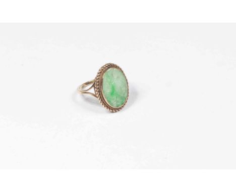 A carved jade type set ring, the oval stone approx 16mm x 12mm, with a 9ct gold rope border and mount, size O, total gross we