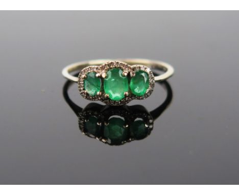 A mid 20th Century Emerald three stone ring, the central emerald 5x4mm flanked by two smaller, surrounds by diamond chips, go