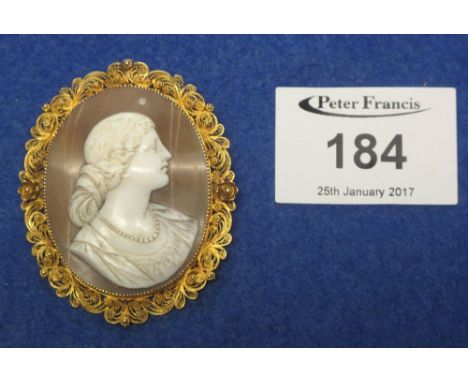 Gold filigree framed portrait shell cameo brooch depicting a young woman with knotted bun in her hair.