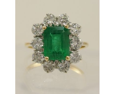 An 18ct emerald and diamond cluster ring the step cut emerald is approximately 2.10cts, and four claw set surrounded with ten