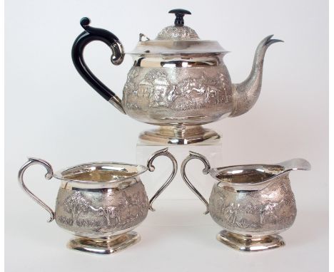 A Burmese silver three piece tea service embossed and chased with village scenes on a matt surface, teapot 25cm high, sugar b