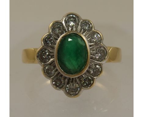 An 18ct emerald and diamond ring the central oval cut emerald is rub over set in yellow gold the diamond are set in a white g