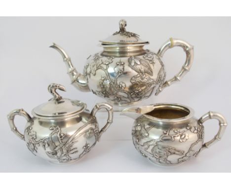 A Chinese silver three piece tea service by Wang Hing decorated with birds amongst flowering branches with faux bamboo handle
