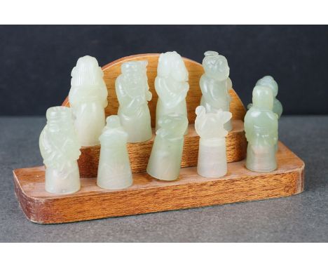 A group of ten carved jade oriental figures on wooden stand. 