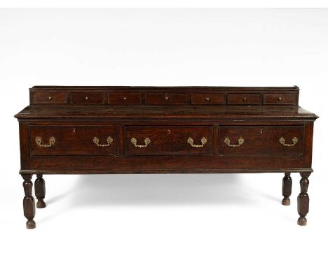 An 18th Century oak dresser base, the raised back having seven drawers over three long drawers, with brass handles and on sha