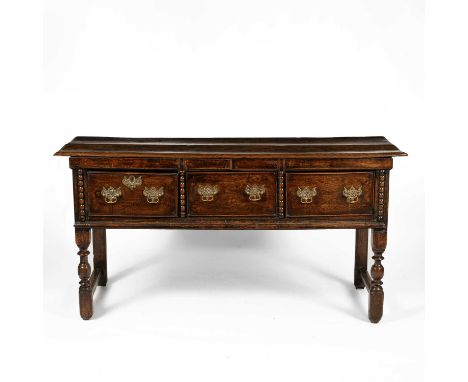 An early 18th Century oak dresser base, the rectangular top with three short drawers and bobbin turned uprights, on turned le