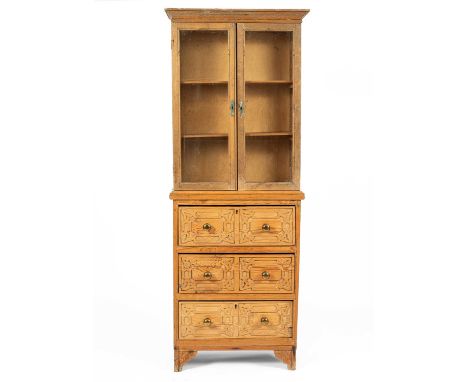 A pine bookcase enclosed by glazed doors on an associated chest of three drawers with strapwork decoration to the drawer fron