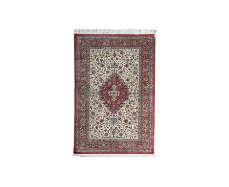A fine silk Qum rug Central Persia, the ivory field of scrolling floral vines centred by a rose pink pendant medallion, frame