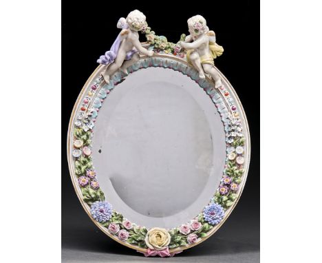 A German oval floral encrusted dressing mirror, early 20th c, crested by putti with flowers, 22.5cm h, backed on wood, underg