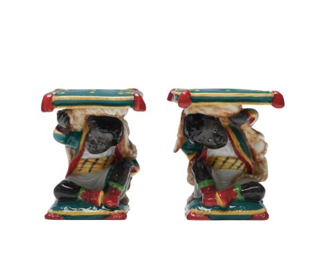 Pair of Royal Doulton prototype porcelain candlestick holders modeled as seated boys supporting square cushion tops. Each fig
