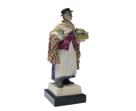 Hand-painted ceramic figure depicts a flower seller standing on a square plinth base. She is dressed in a long white dress wi