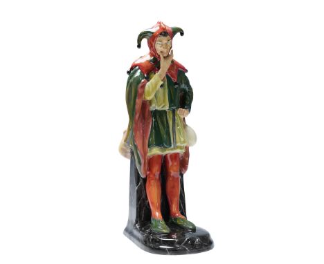 Modeled as a jester standing in a theatrical pose with one hand resting on his chin. The figure is dressed in a green tunic w