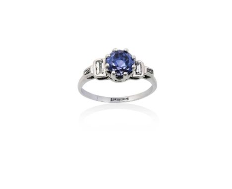 A Sapphire and Diamond Ringthe round cut sapphire in a white claw setting, to baguette cut diamond set shoulders in rubbed ov