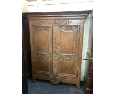 A French floral carved oak armoire, the moulded cornice above two panel doors with brass escutcheons and hinges, enlosing two