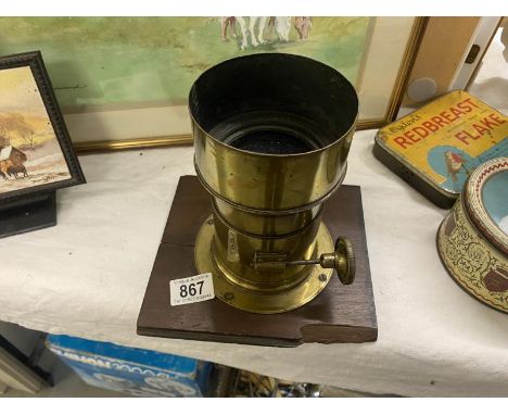 A large brass camera/magic lantern lensLens shield 10.6cm diameter.Lens approximately 8cm.Total height 18.5cm.Damaged wood ba