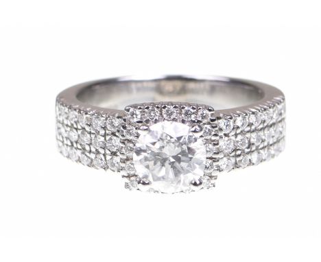 A diamond dress ringCentring a round brilliant cut diamond, to a round brilliant cut diamond surround and shoulders, to a pla