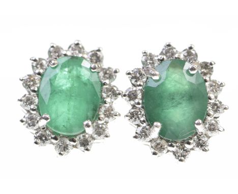 A pair of emerald and diamond cluster ear studsThe oval shaped emerald, within a round brilliant cut diamond surround, to ear