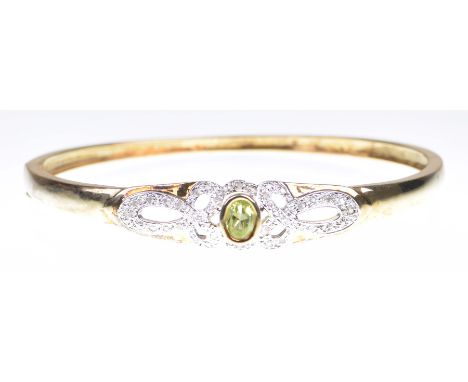 A peridot and diamond set bangleThe oval shaped peridot, bezel set, set between diamond set openwork scrolls, to a 9k gold hi