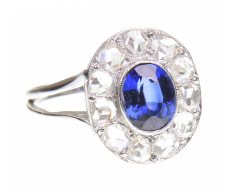 A sapphire and diamond cluster ringCentring an oval shaped sapphire, possibly synthetic, to a rose-cut diamond surround, in u