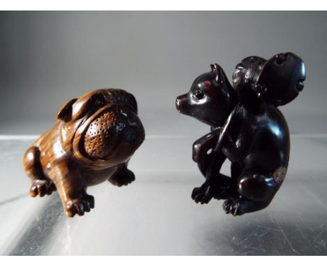 Netsuke - two vintage dark wood Japanese netsukes, one in a form of a Pug dog, the other depicting a dog, carrying a heavy lo