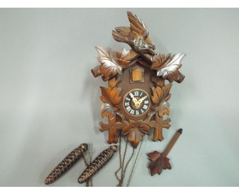 A Black Forest cuckoo clock, wall mounted in a case carved with leaves and surmounted by a cuckoo, matching leaf to the pendu