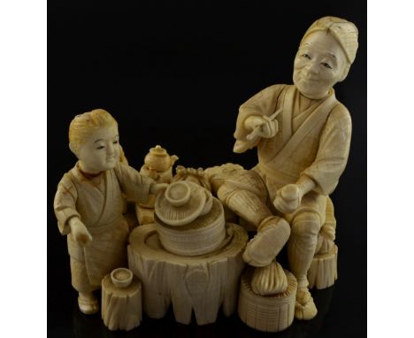 19th century Japanese ivory okimono, a seated man smoking a pipe with a boy in a kitchen, Meiji period, 21 cms wide x 18 cms 