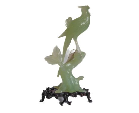 A large and elaborate Chinese light-green hardstone carving of a crested bird perched upon a gnarled branch with two leaves e