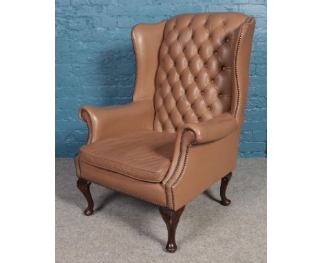 A pale brown button back wing armchair, with brass studs on carved cabriole legs and leather upholstery. H:,W:,D:  One of the