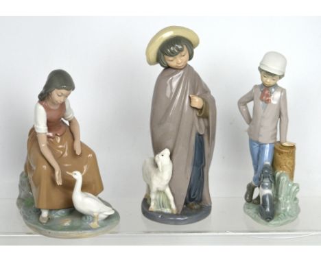 Three Nao figural groups comprising a seated girl feeding a goose, a cloaked boy with lamb and a young boy with seated dog (3