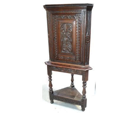 An early 20th century carved oak free-standing corner cupboard, single-door cupboard raised on turned legs over shelf, width 