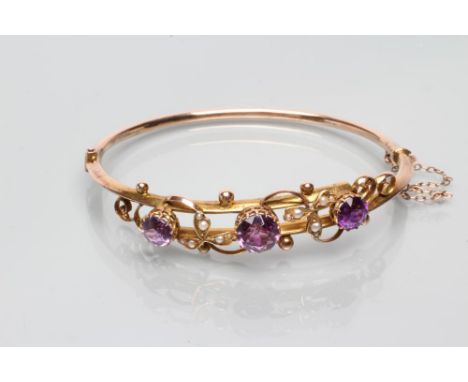 AN EDWARDIAN STIFF HINGED BANGLE, the upper section with two hollow bars tied by three open back collet set amethysts with se