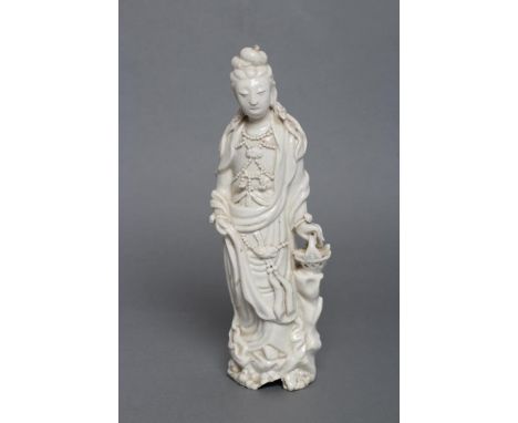 A CHINESE BLANC DE CHINE PORCELAIN FIGURE modelled as a female deity wearing a beaded bodice, her left hand resting on a bask