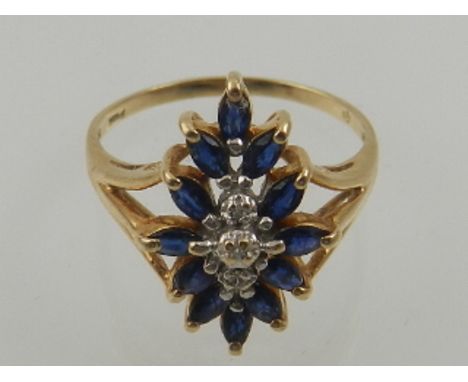 A 10 carat yellow gold, diamond, and sapphire cluster ring, set a line of diamond accents surrounded by twelve marquis cut bl