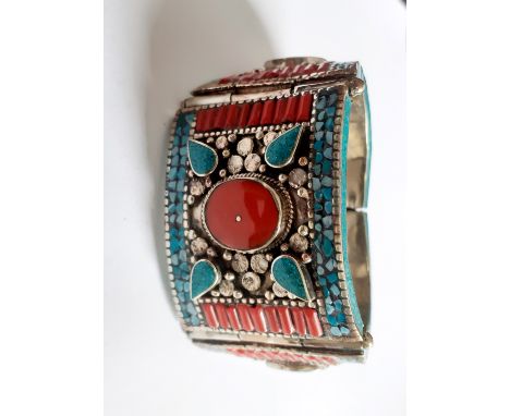 A Tibetan white metal tribal bangle set with turquoise, coral and other stones, Dia. 6cm.