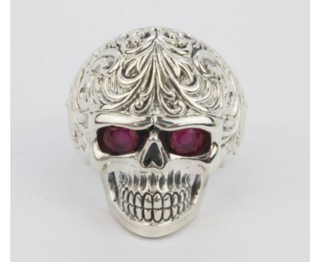 A 925 silver skull shaped ring with oval cut ruby set eyes, (R).