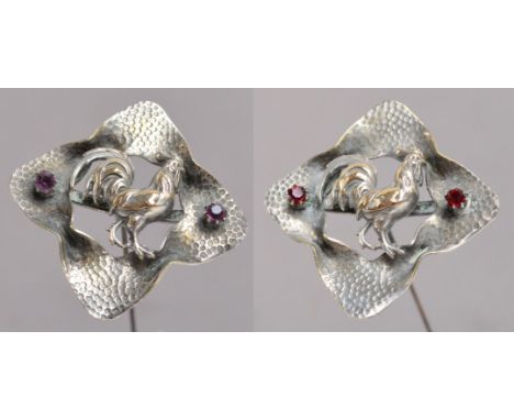 A pair of large hammered effect metal hat pins, each decorated with a cockerel in a shaped square setting, one with ruby colo