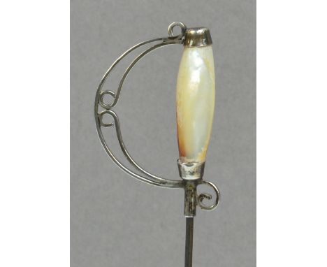 A white metal hat pin in the form of a sword hilt with mother of pearl grip, height of head 3cm, on 18.7cm pin.