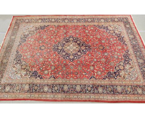 A LARGE RED GROUND KESHAN RUG with all over floral foliate design, dark blue central medallion, matching spandrels and a dark