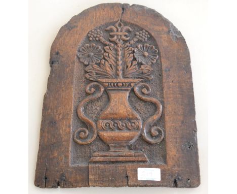 < A carved oak arched panel, 17th century, carved with a vase of flowers, 38cm by 28cm