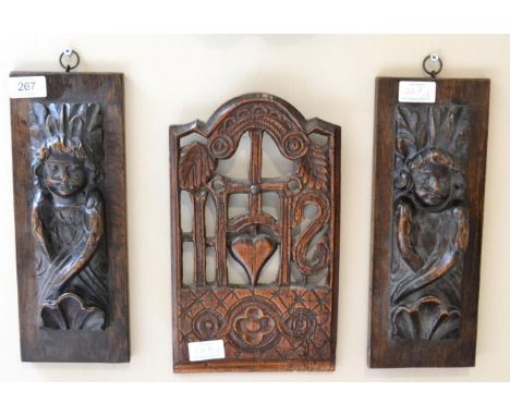 < A pair of carved oak figures of angels, 17th century, with shell terminals, 23cm by 8cm, on later panels; and a carved and 