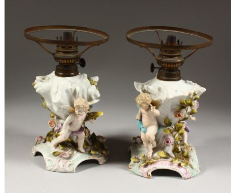 A PAIR OF CONTINENTAL PORCELAIN LAMP BASE, with cupids and encrusted with flowers. 9ins high.