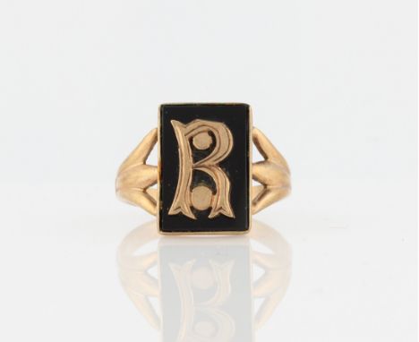 A memorial ring, set with a rectangular piece of black hardstone, surmounted with the initial R, in unmarked yellow metal.
