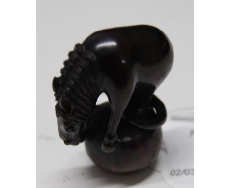 A 20thC carved wood Japanese netsuke, a study of a horse stood balanced on a sphere with a wood ring hooped around its hind l